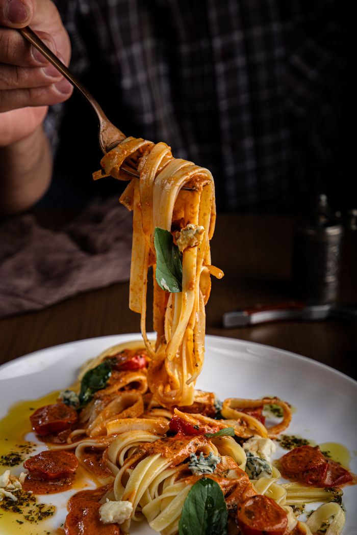 Close-up of a fork twisting linguine pasta in rich tomato sauce with basil and cheese.
