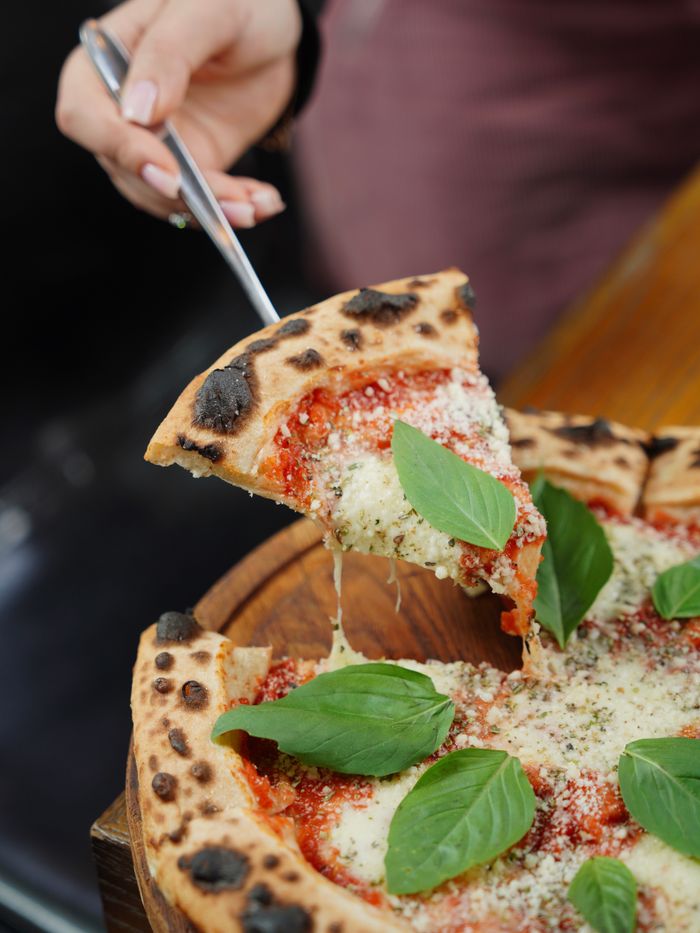 Delicious pizza slice being served, topped with fresh basil and molten cheese.