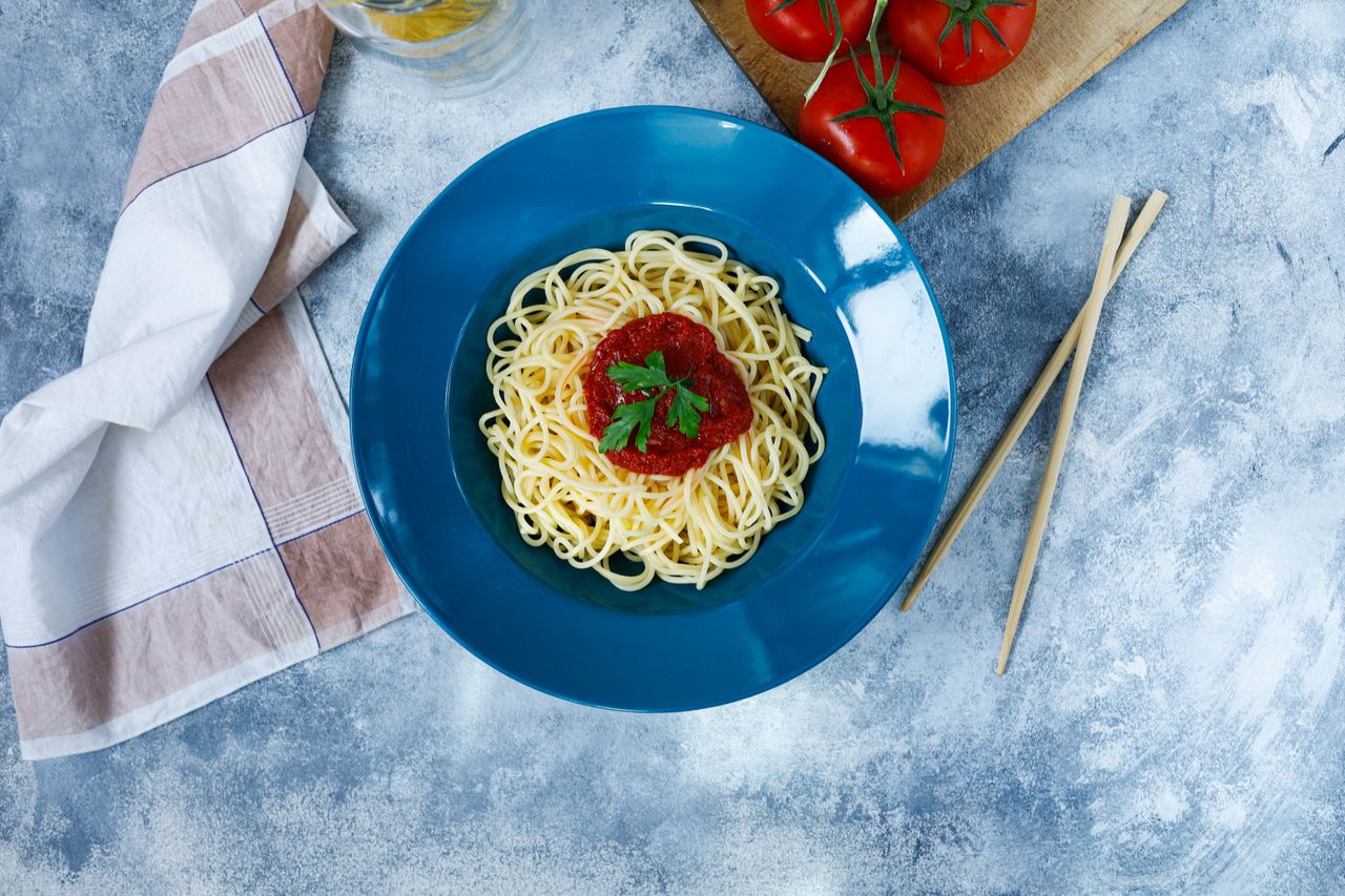 Top view of spaghetti with tomato sauce garnished with parsley, served on a blue plate.