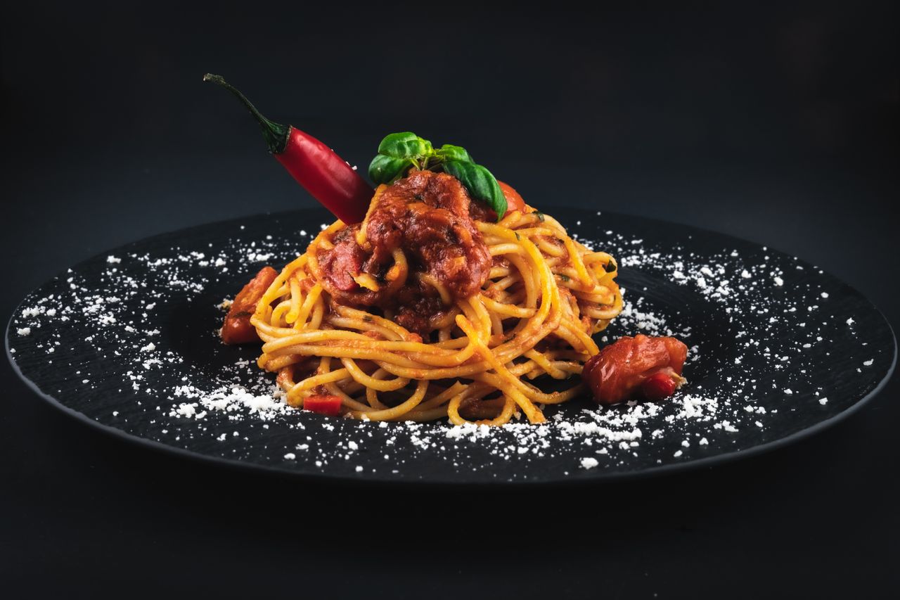 Close-up of spicy spaghetti with tomato sauce and garnished with basil on a dark plate.